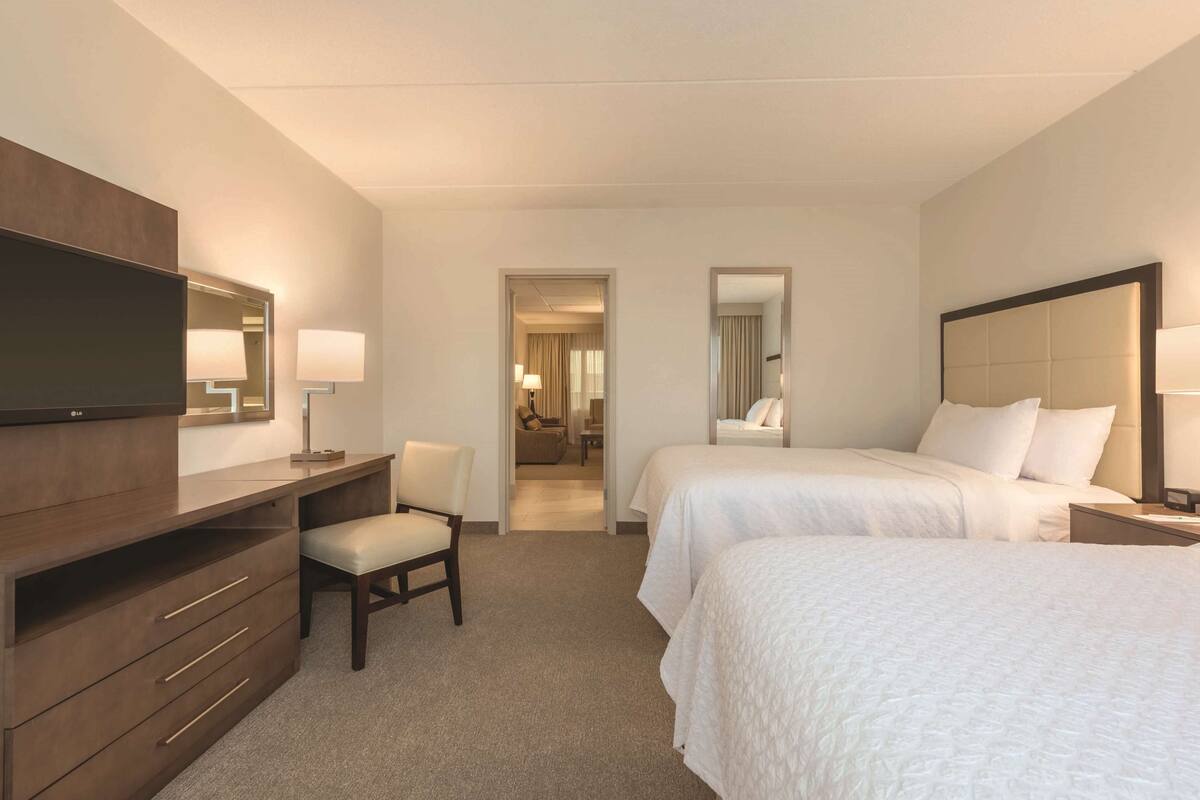 Une chambre d’hôtel avec un lit, un bureau et une chaise, un téléviseur et une salle de bain visible à travers une porte ouverte.