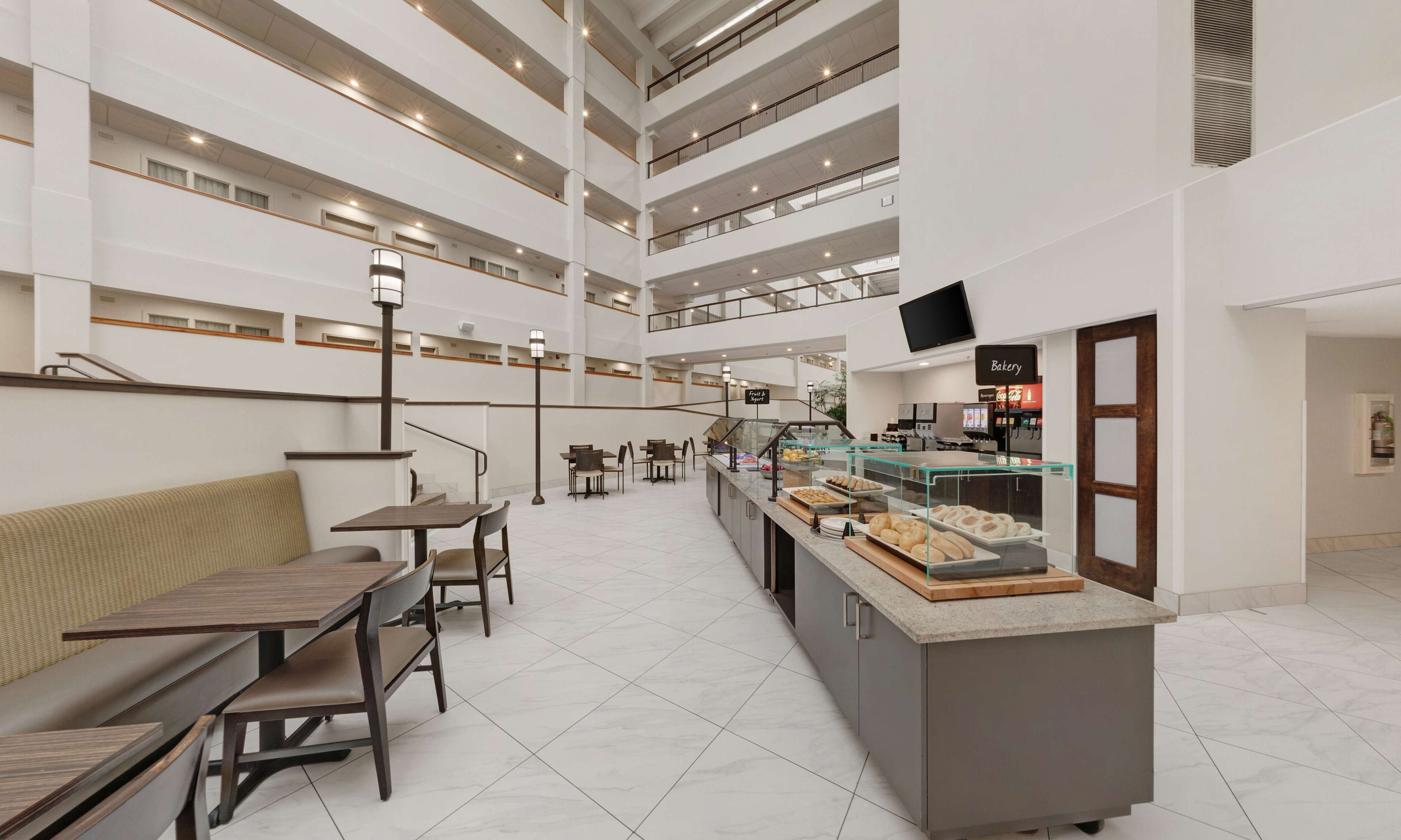 A multi-level hotel lobby with a central food service area, seating arrangements, and a bakery.
