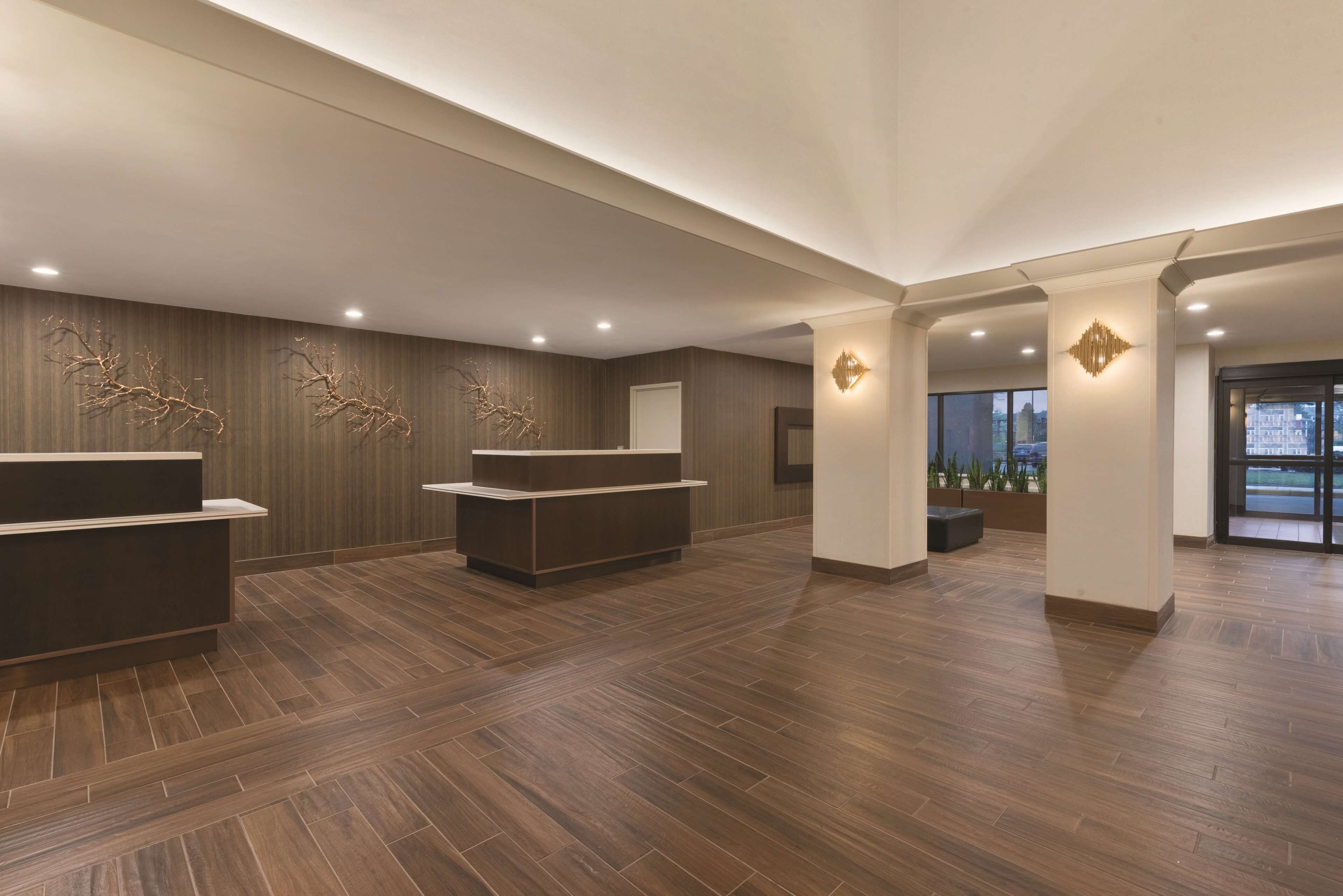 A spacious lobby with a wooden floor, reception desks, and modern wall decor.
