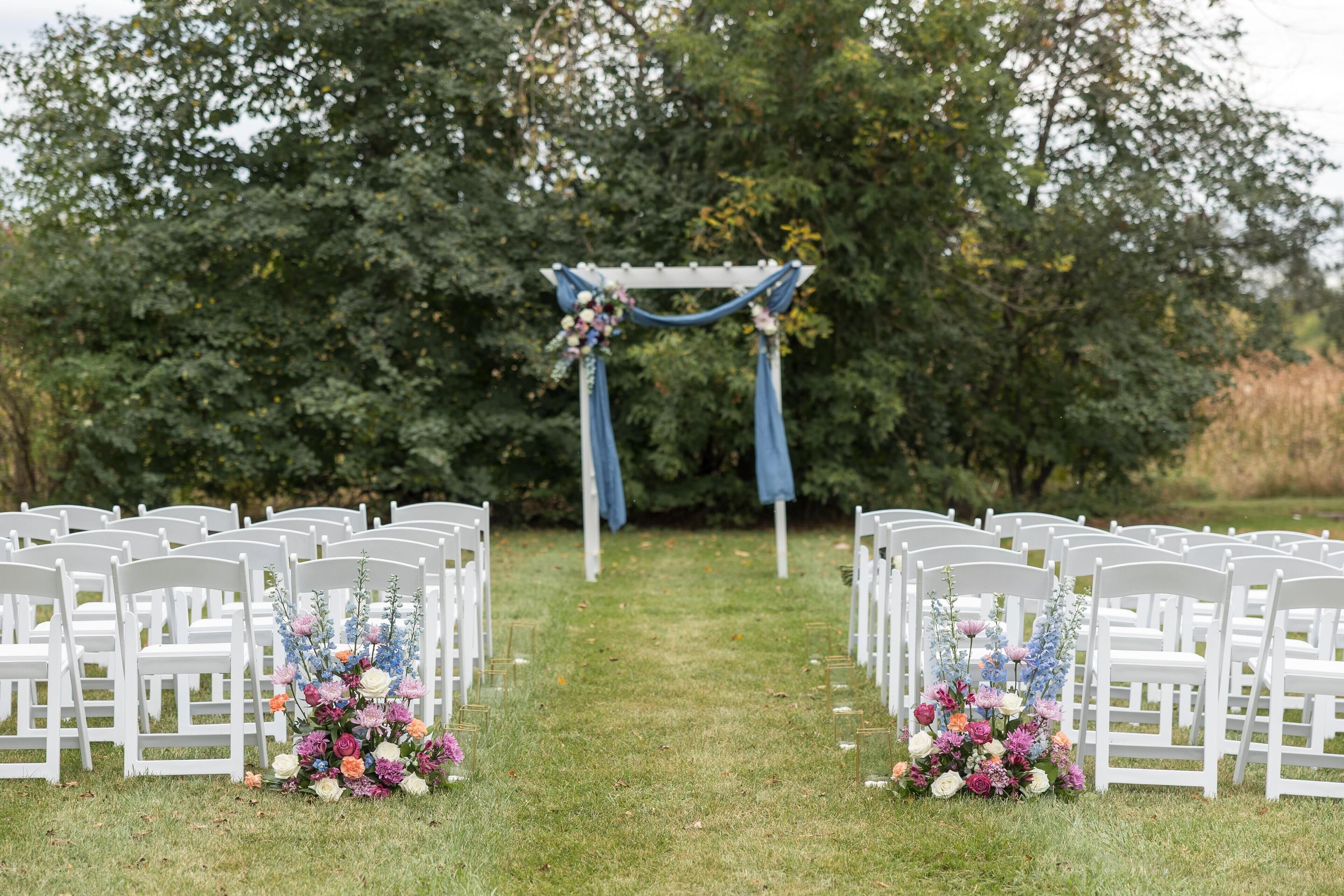 En vit trägång med stolar på vardera sidan, som leder fram till en blå båge dekorerad med blommor.