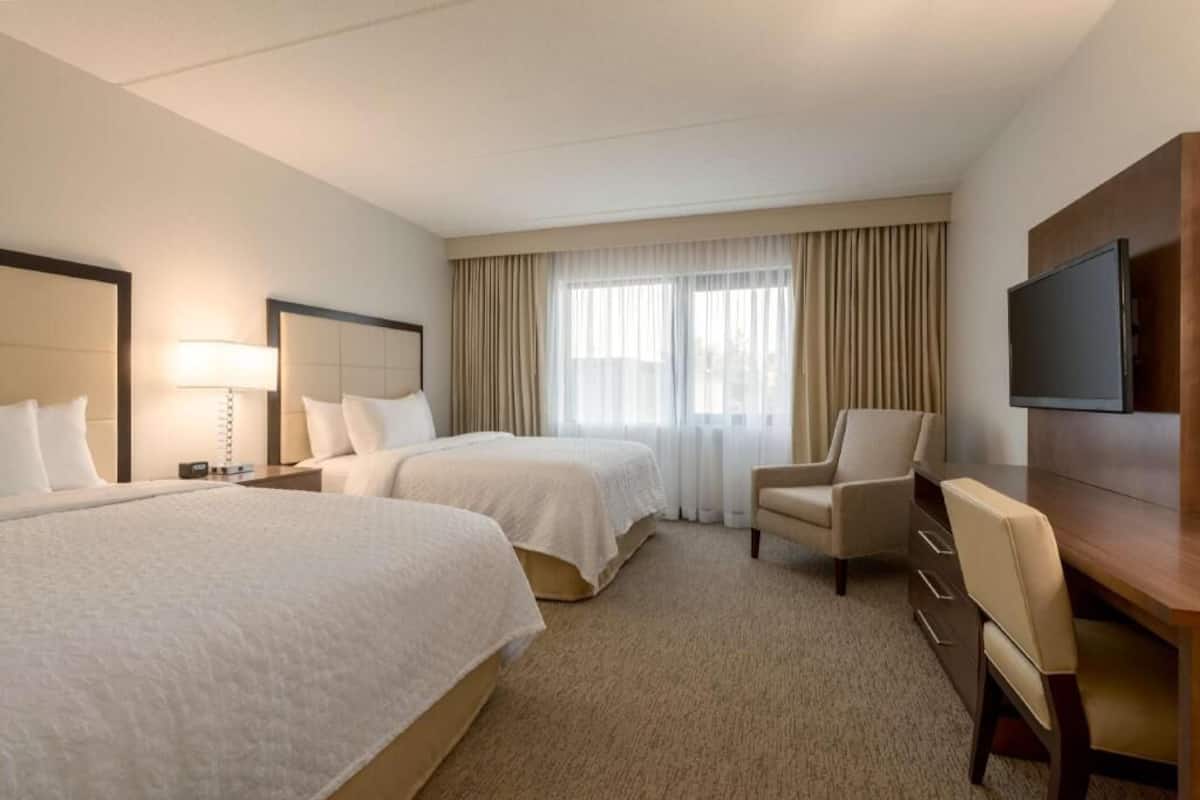 Une chambre d’hôtel avec deux lits, un bureau, une chaise, une télévision et une grande fenêtre avec des rideaux.