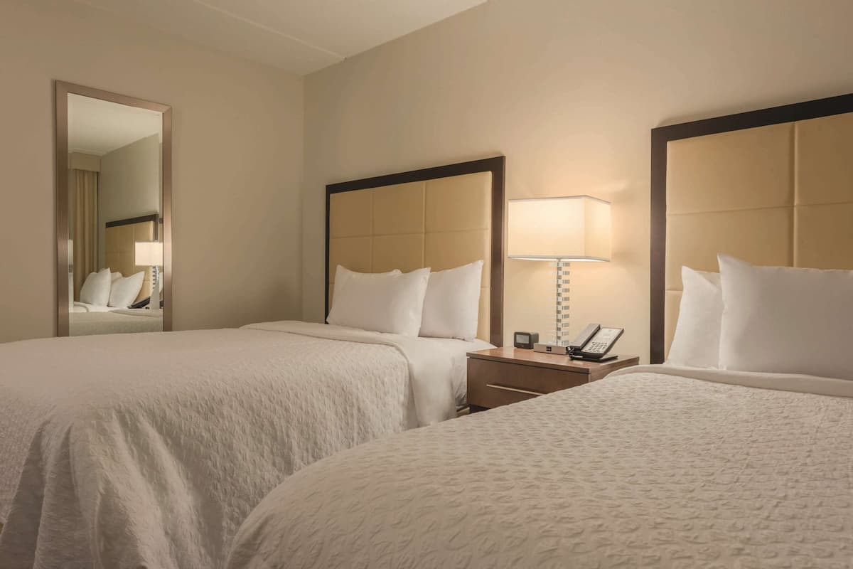 Une chambre d’hôtel avec deux lits, une table de chevet avec une lampe et un miroir.