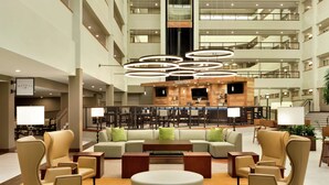 A spacious lobby with a central seating area, a bar, and a staircase leading to upper floors.