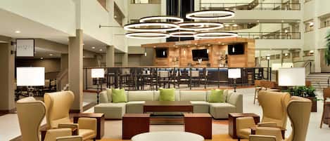 A spacious lobby with a central seating area, a bar, and a staircase leading to upper floors.
