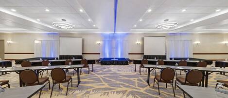 A conference room with a long table, chairs, a stage, and a carpeted floor.