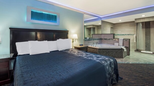 Habitación de hotel con una cama grande, baño independiente con bañera y un espejo que refleja la habitación.