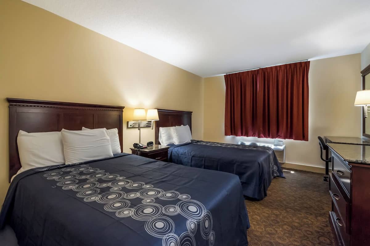 A hotel room with two beds, a desk, a chair, a dresser, and a window with curtains.
