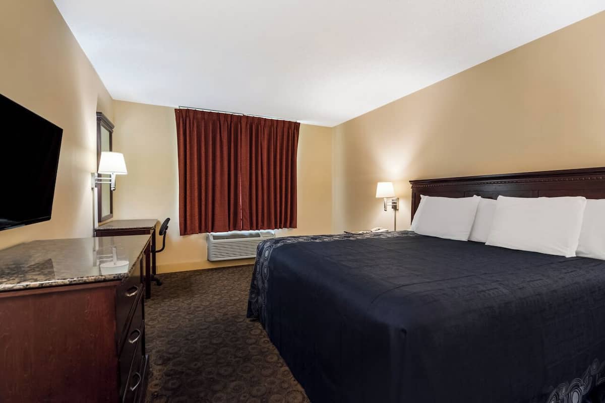 A hotel room with a bed, a desk, a chair, a TV, and a window with curtains.