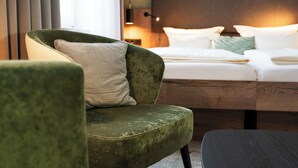 A hotel room with a green armchair, a wooden bed frame, and a bedside table.