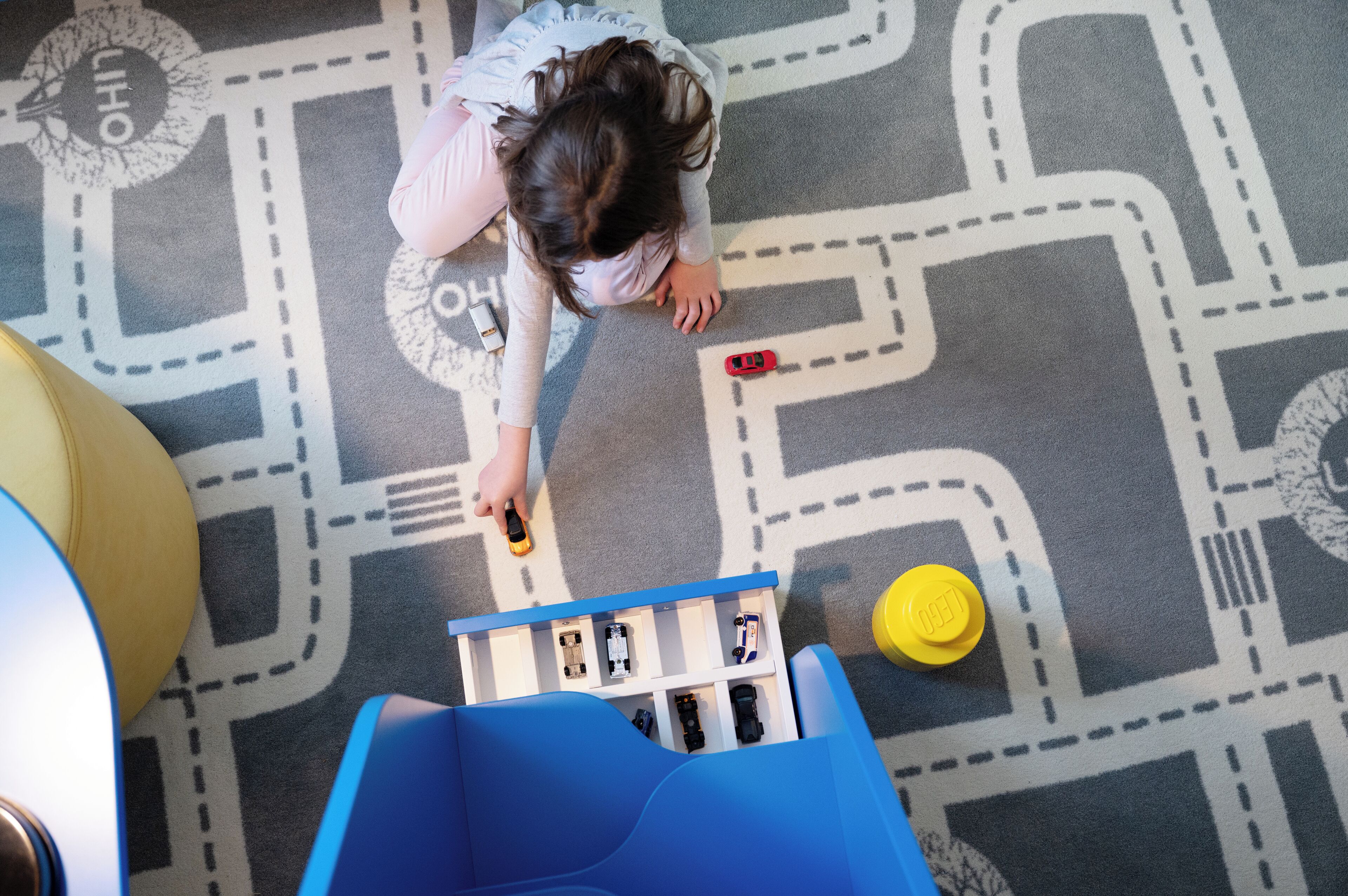 Een kind speelt met autootjes op een speelkleed met een patroon.