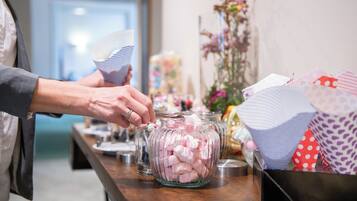 A person filling a glass jar with pink marshmallows from a container.