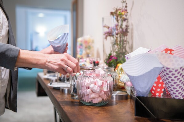 A person filling a glass jar with pink marshmallows from a container.