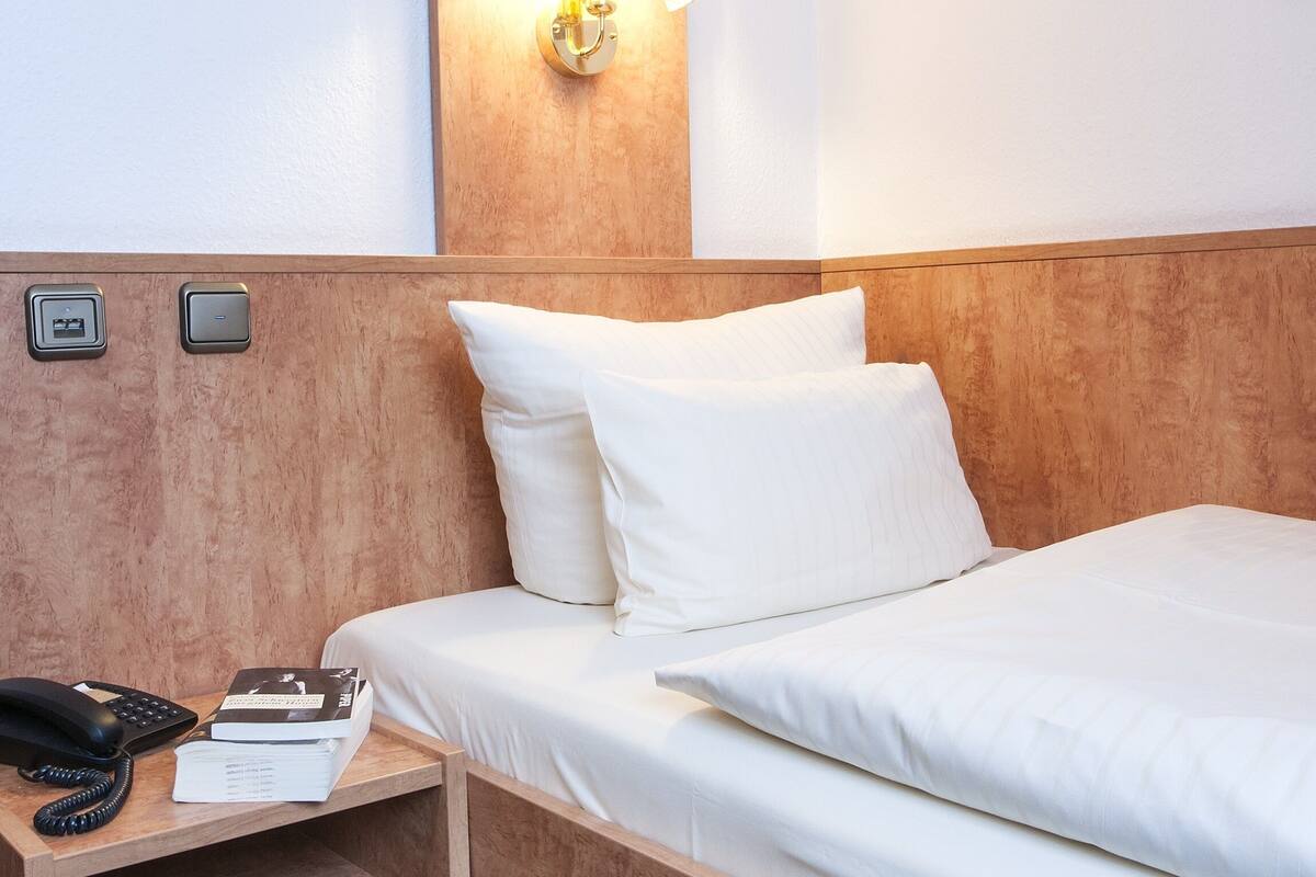 Habitación de hotel con cabecera de madera, lámpara de noche, teléfono, bloc de notas y una alfombra azul estampada.