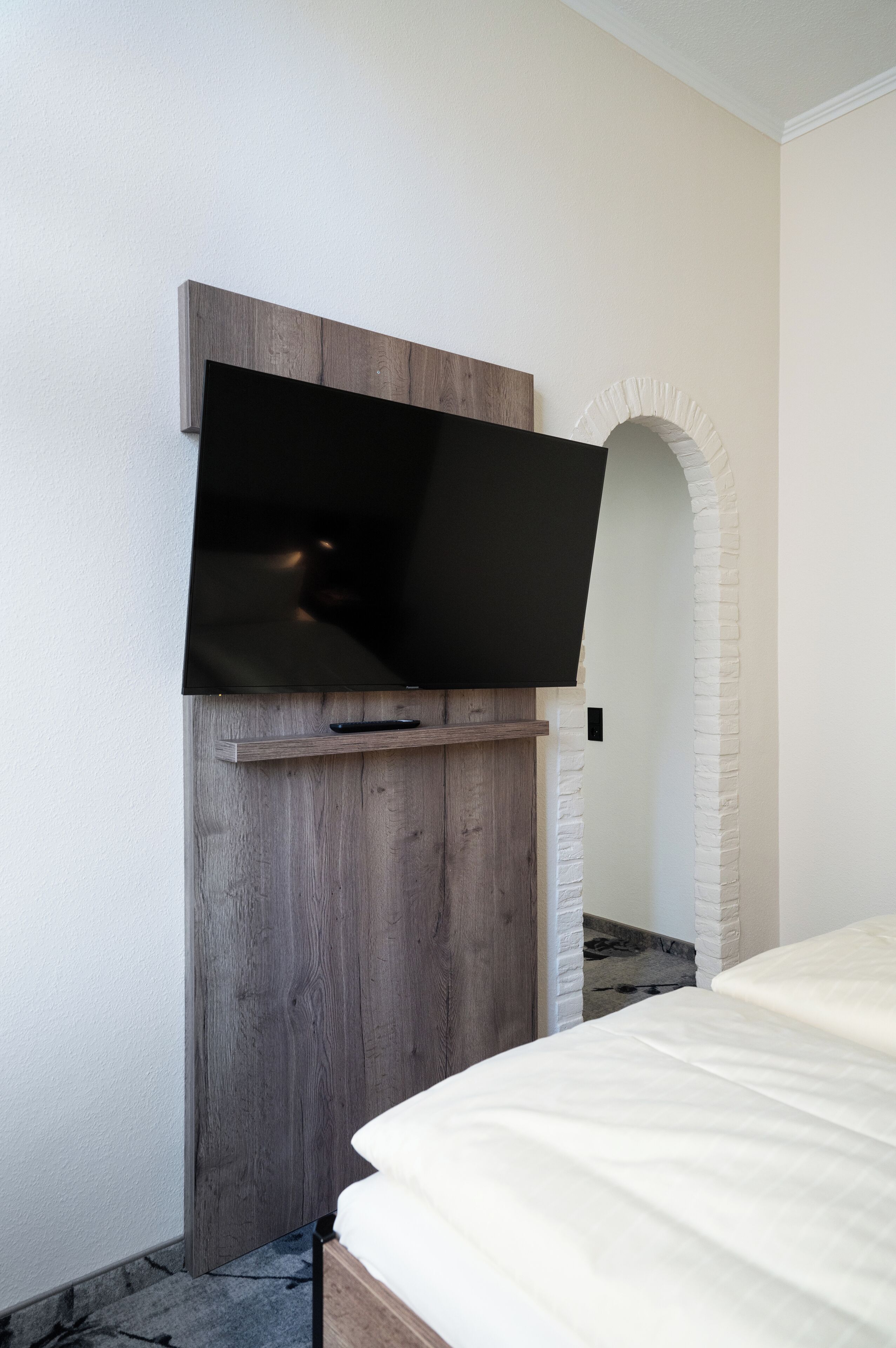 A bedroom with a mounted TV, a wooden headboard, and a white archway.
