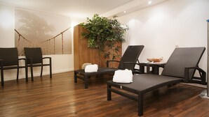 A room with wooden flooring, wicker lounge chairs, a small table with a bowl, and a large plant.