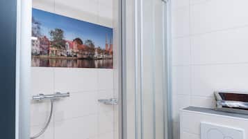A modern bathroom with a glass shower enclosure, a toilet, and a wall-mounted control panel.