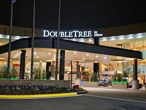 Entrada de um hotel com uma placa indicando 'DOUBLETREE by Hilton' e uma área coberta com colunas.
