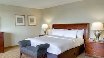 A hotel room with a large bed, two bedside lamps, a chair, a wooden dresser, and two framed pictures on the wall.