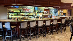A bar area with a long counter, multiple stools, and a mural on the wall. - DoubleTree by Hilton Washington Dulles Airport (Herndon)
