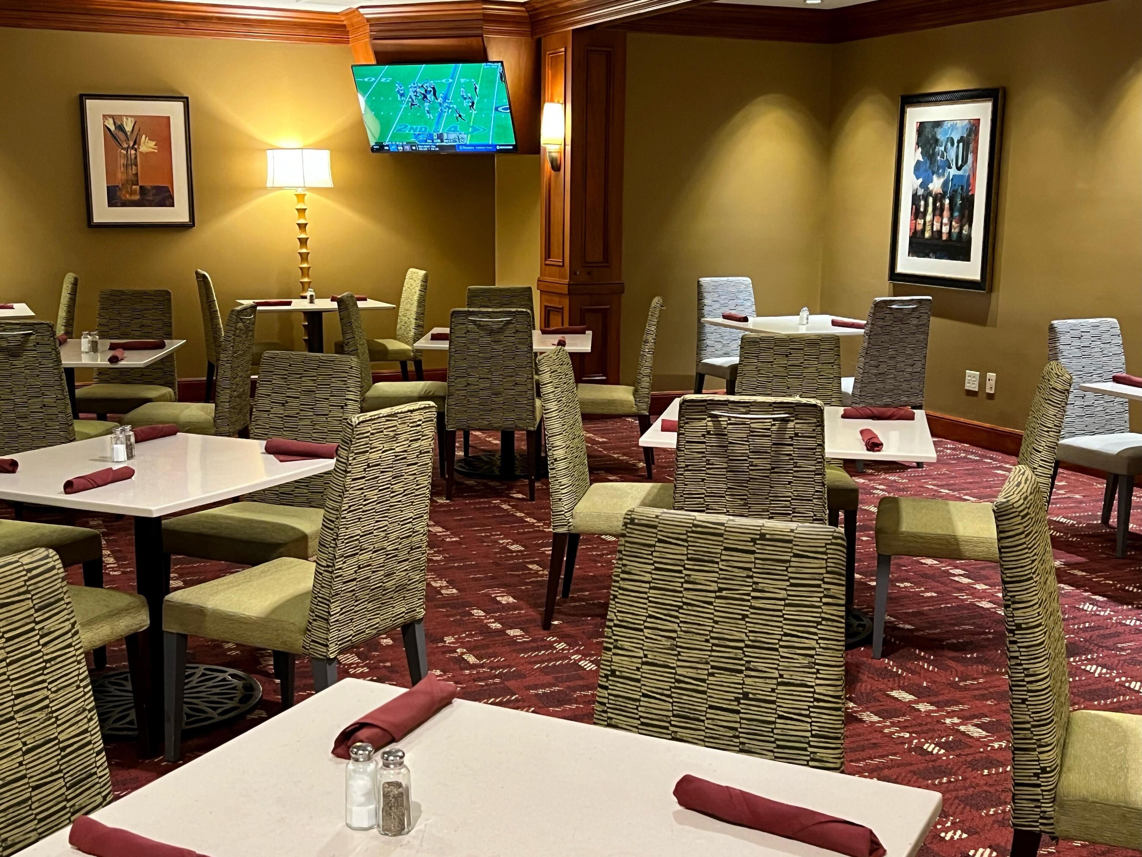 A hotel dining area with wicker chairs, white tables, and red napkins.