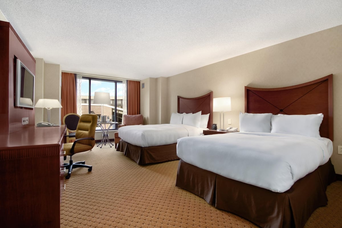 Een hotelkamer met twee bedden, een bureau, een stoel en een groot raam.