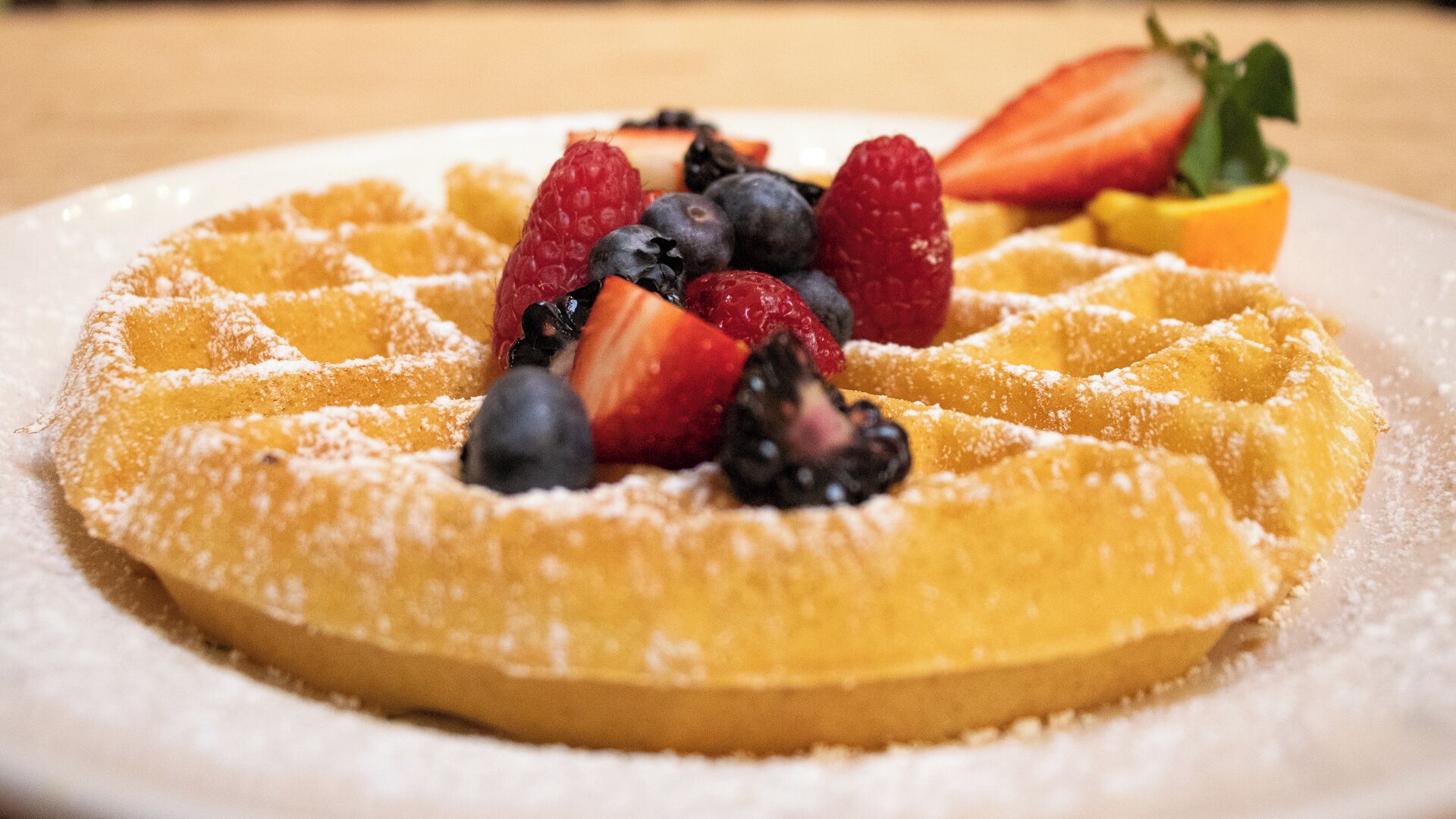 Um close-up de um waffle belga com açúcar em pó e frutas vermelhas frescas.
