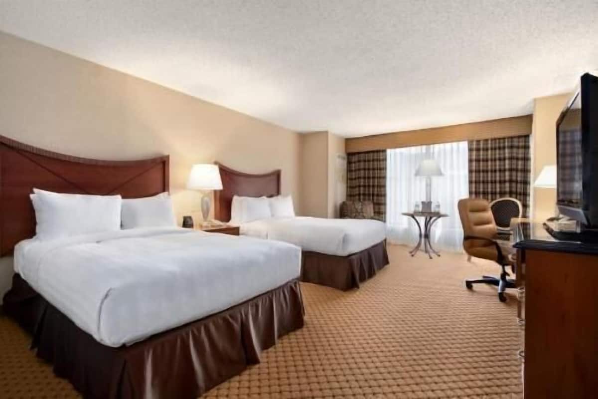 Een hotelkamer met twee bedden, een bureau, een stoel, een televisie en een raam met gordijnen.