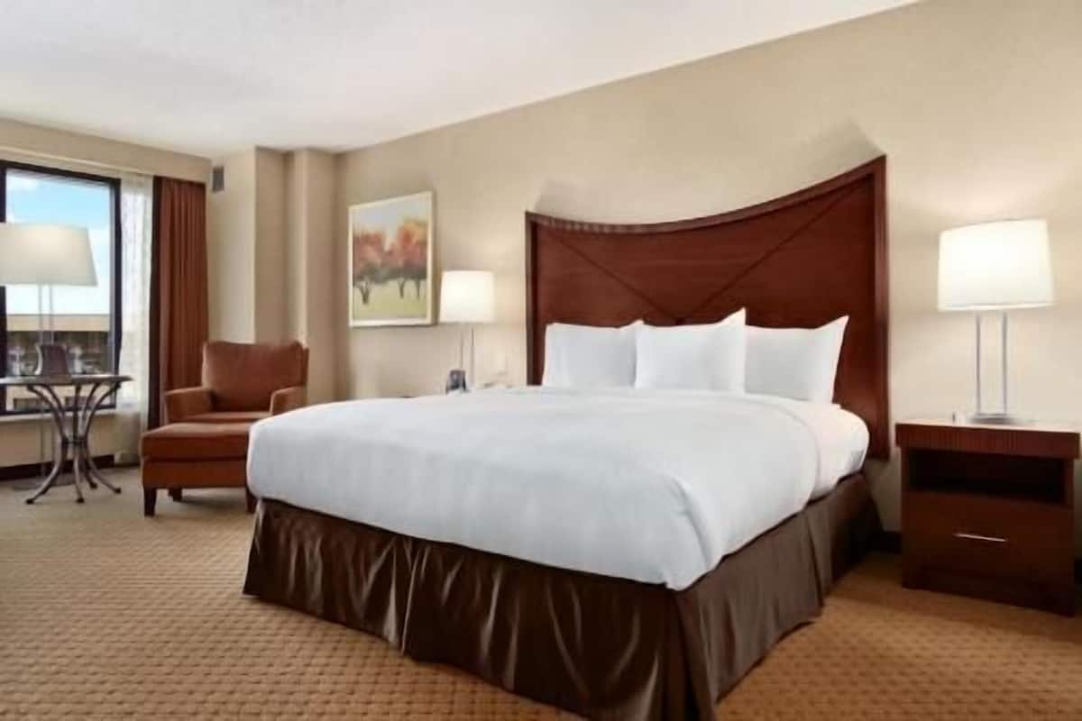Een hotelkamer met een groot bed, een bureau, een stoel en een schilderij aan de muur.