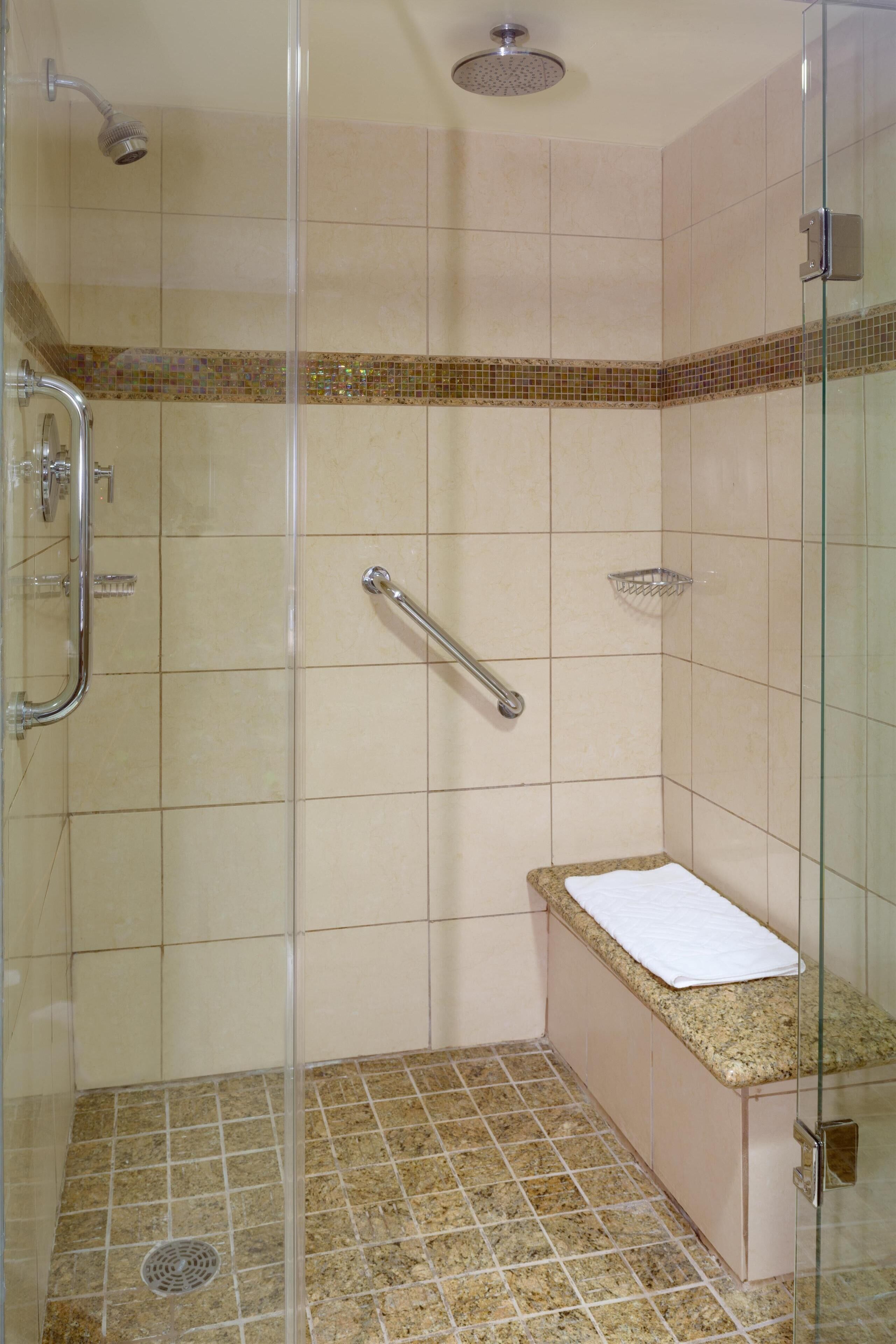 A shower with a glass door, a handrail, and a small bench with a towel.