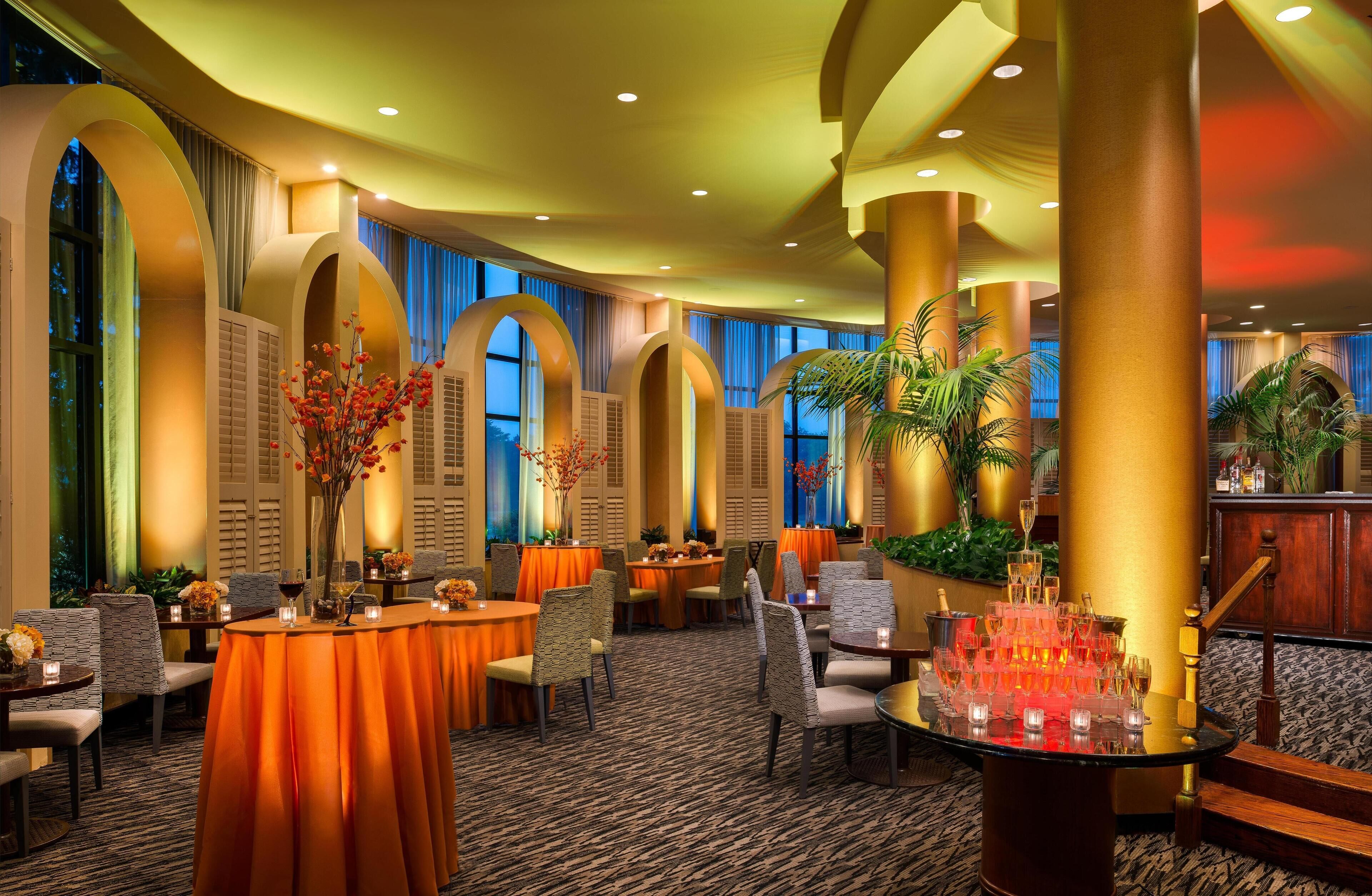 A hotel lobby with round tables, chairs, and a bar area.