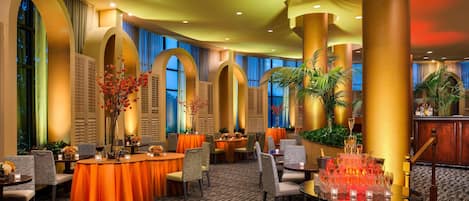 A hotel lobby with round tables, chairs, and a bar area.