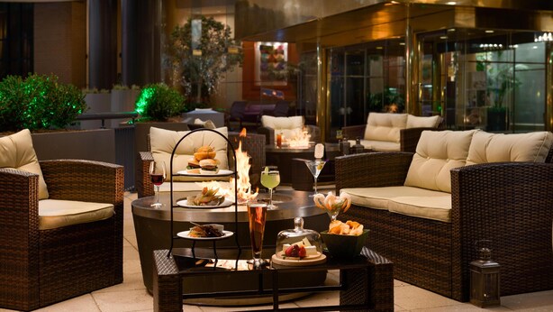A cozy outdoor seating area with wicker furniture, a round table with food and drinks, and a fire feature. - DoubleTree by Hilton Washington Dulles Airport (Herndon)