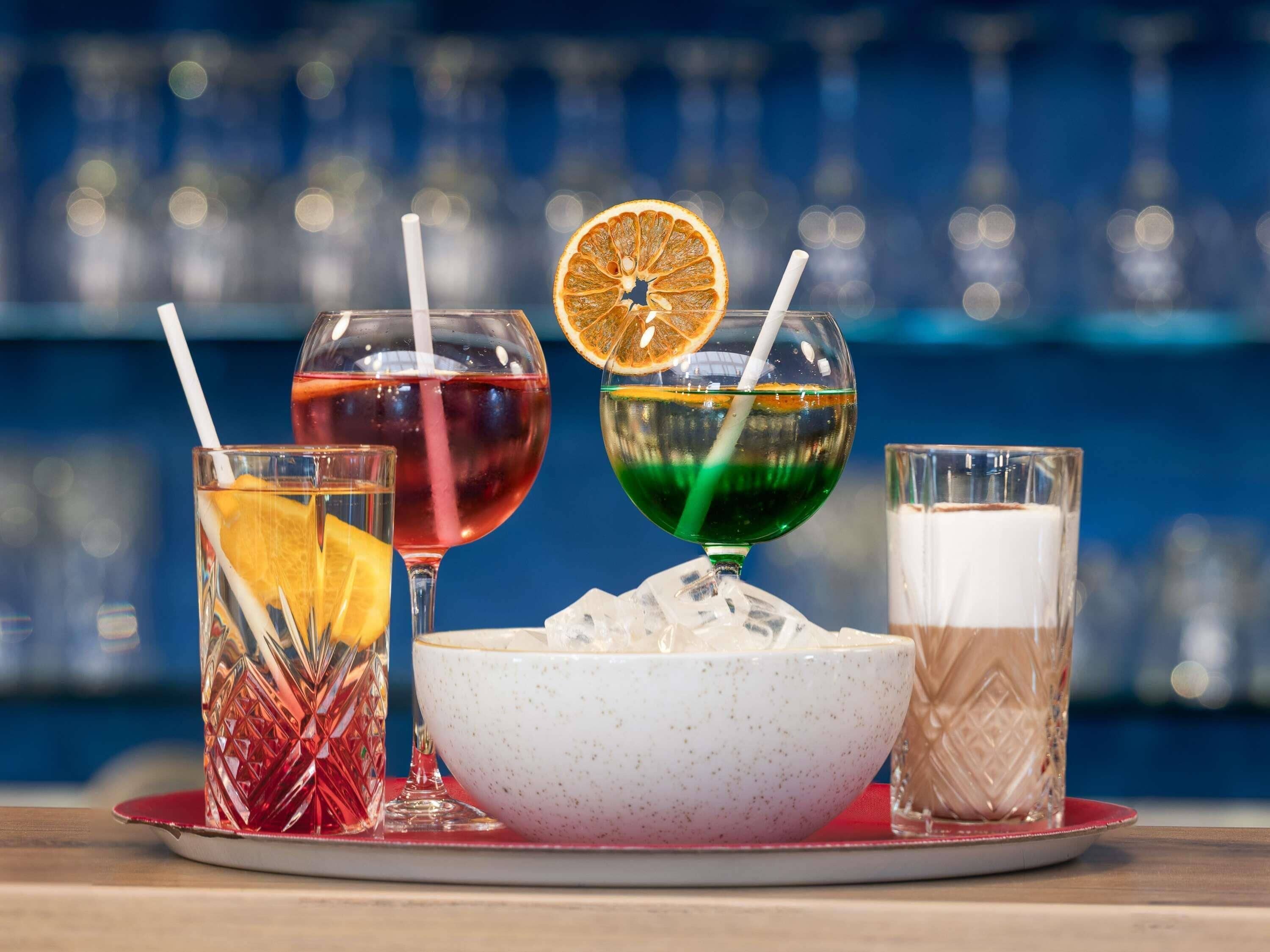 Un bar con diferentes bebidas, incluyendo un cóctel rojo, un cóctel verde, un cóctel blanco y un helado.