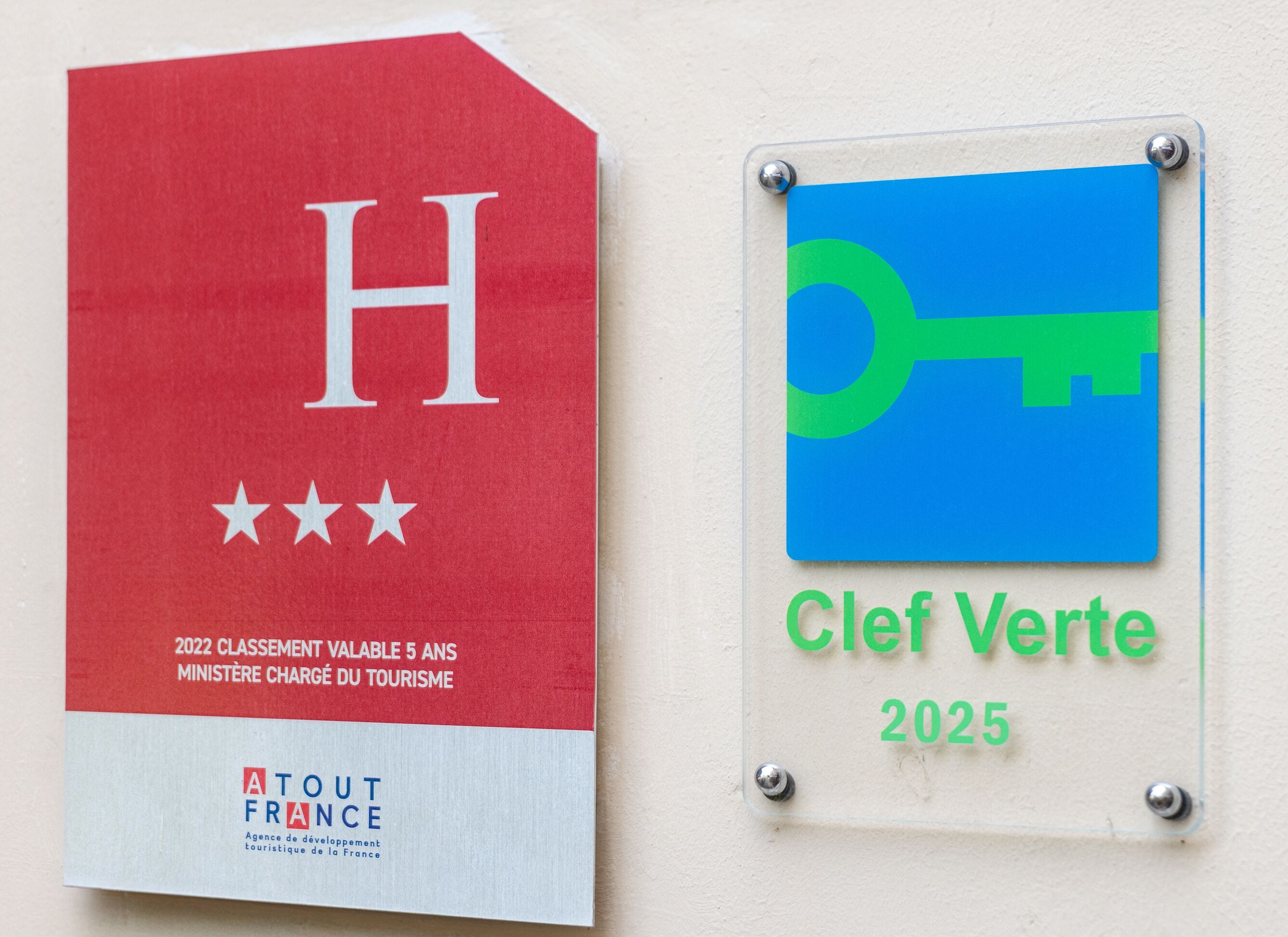 Dos placas montadas en una pared, una roja con una 'H' grande y tres estrellas, y la otra azul con un símbolo de llave verde y el texto 'Clef Verte 2025'.