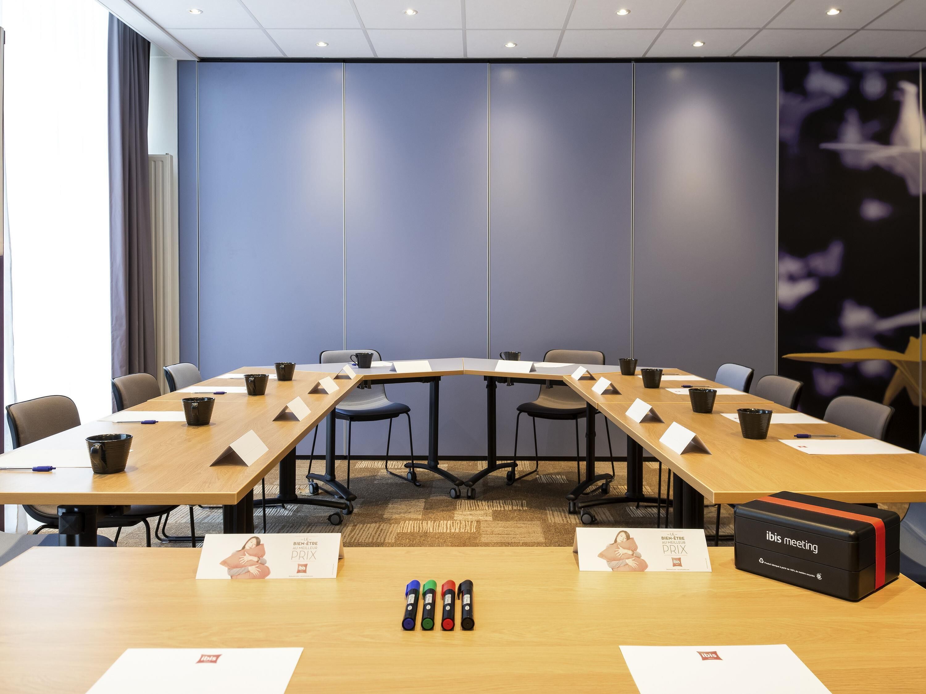 Una sala conferenze con un lungo tavolo, sedie e una scatola nera con la scritta 'ibis meeting' sul pavimento.