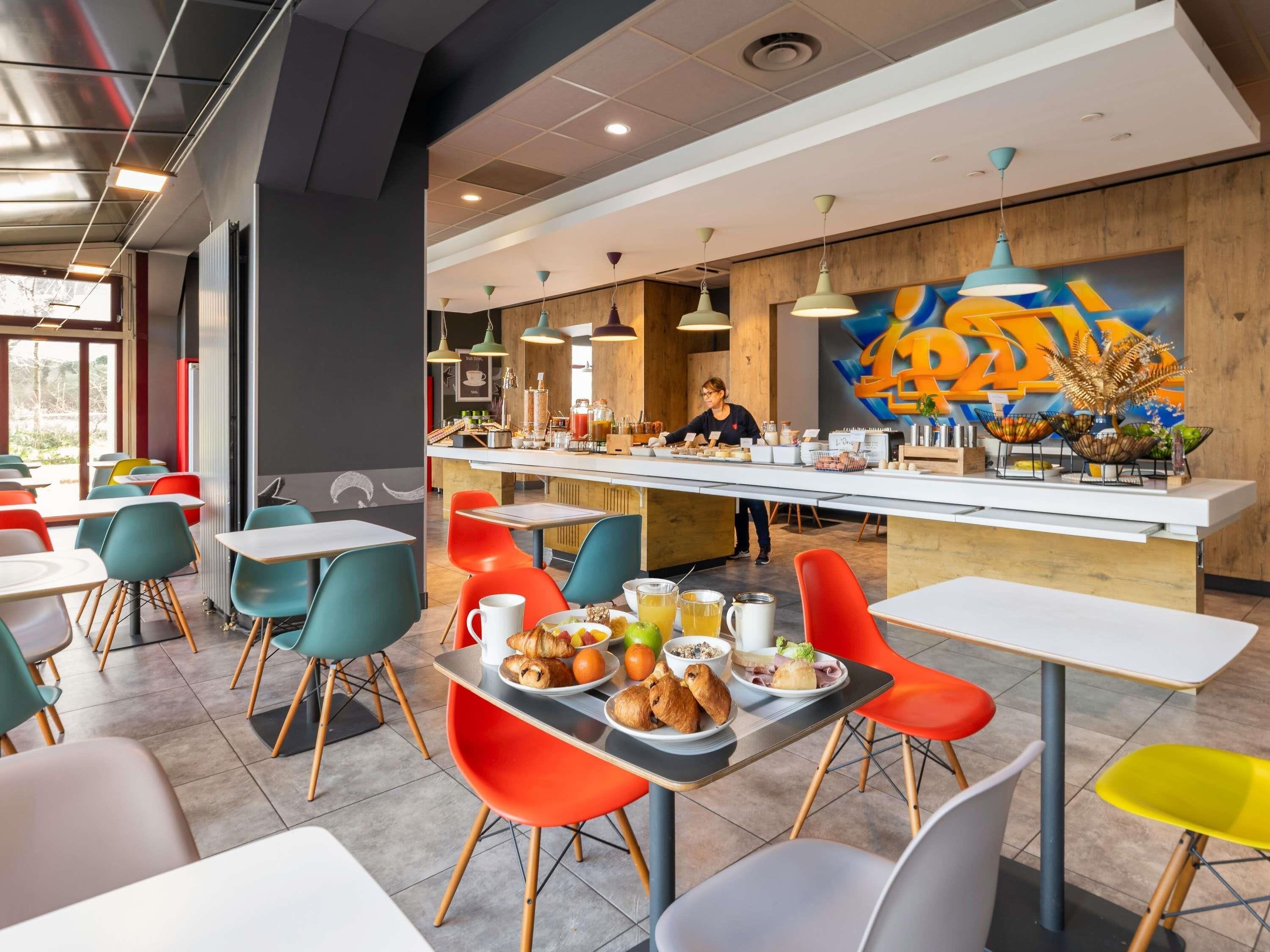 Una cafetería moderna con sillas coloridas, una barra con un barista y un mural vibrante en la pared.