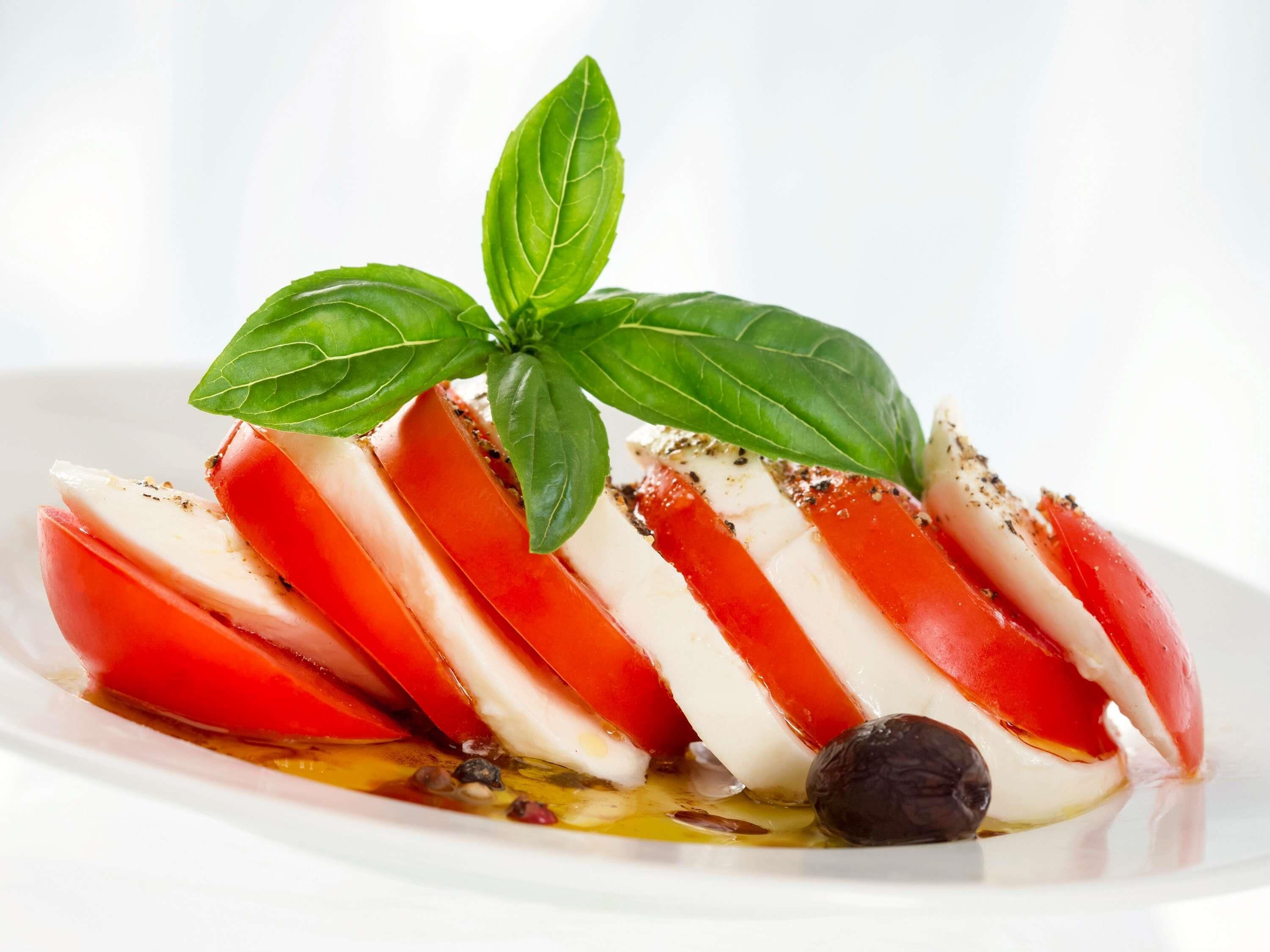 Um prato com fatias de tomate e mussarela, decorado com folhas de manjericão.