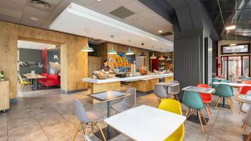 Een modern café met een centrale balie, verschillende zithoeken en een diversiteit aan stoelen en tafels.