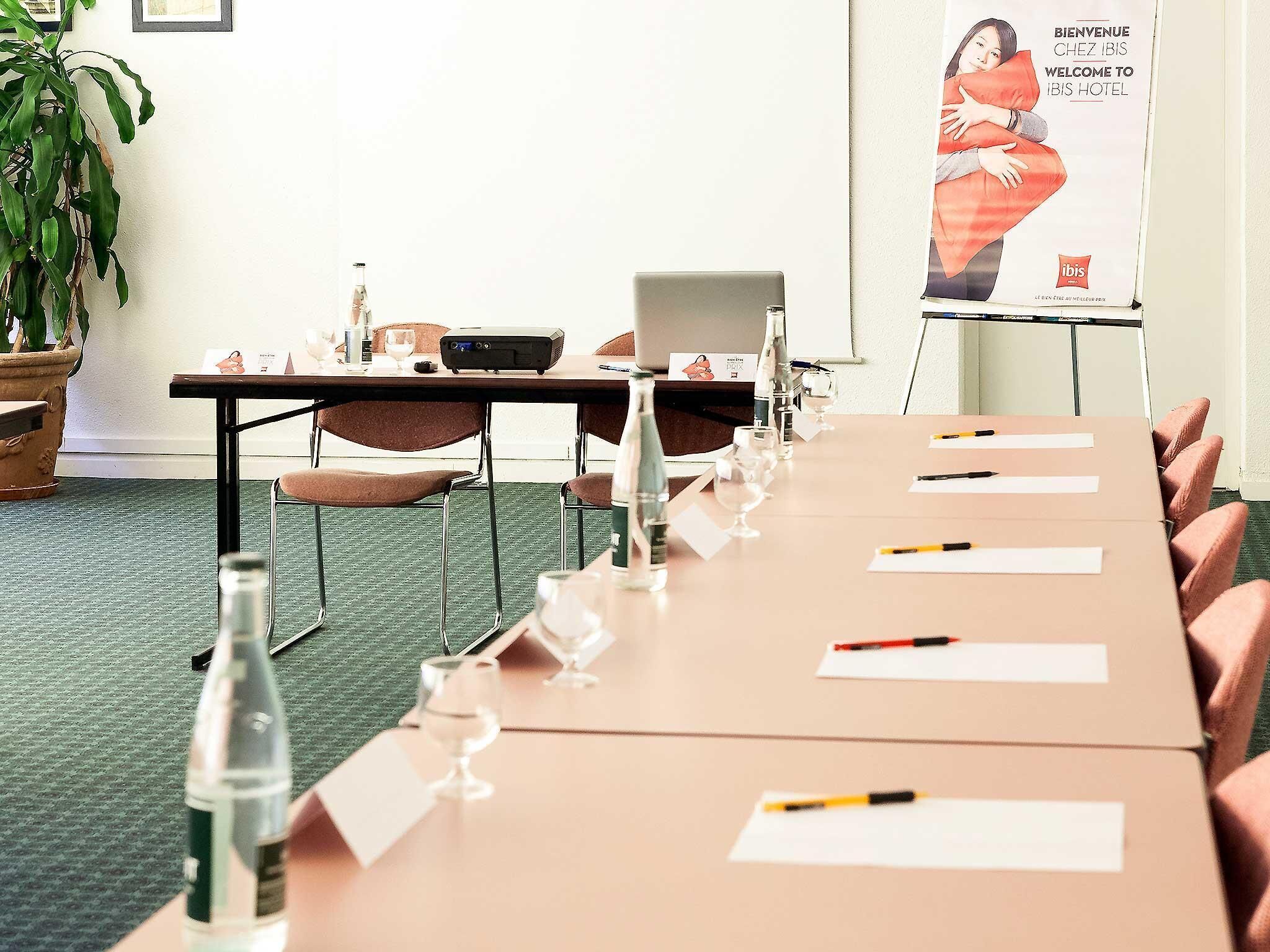 Un salón de conferencias con una larga mesa, sillas, tarjetas de identificación, botellas de agua y una computadora portátil.