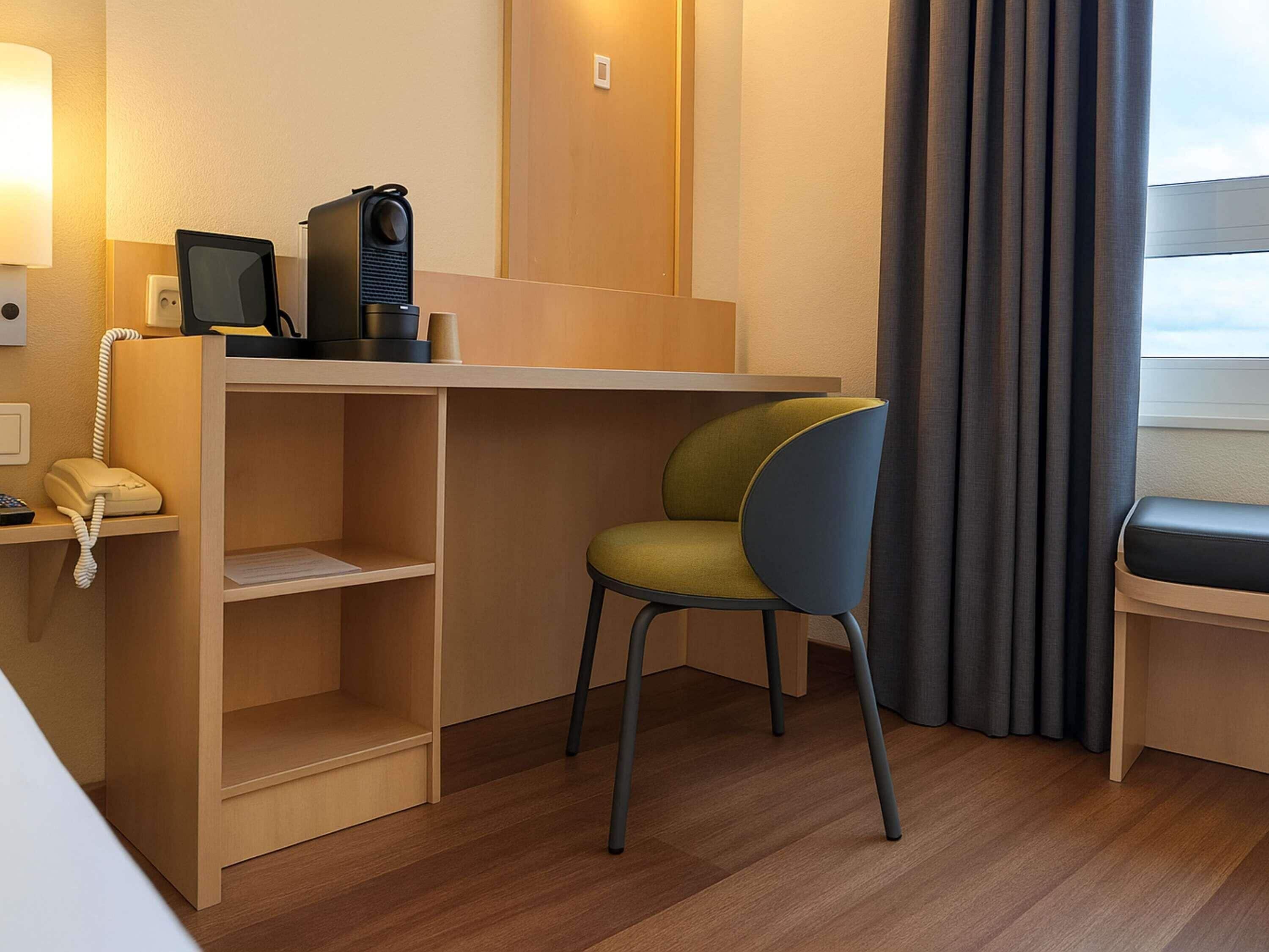 A compact hotel room with a desk, chair, and a telephone.