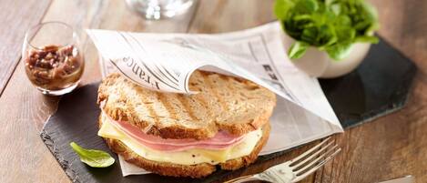 Un sándwich sobre una tabla de piedra negra, con un tenedor y un cuchillo a un lado.