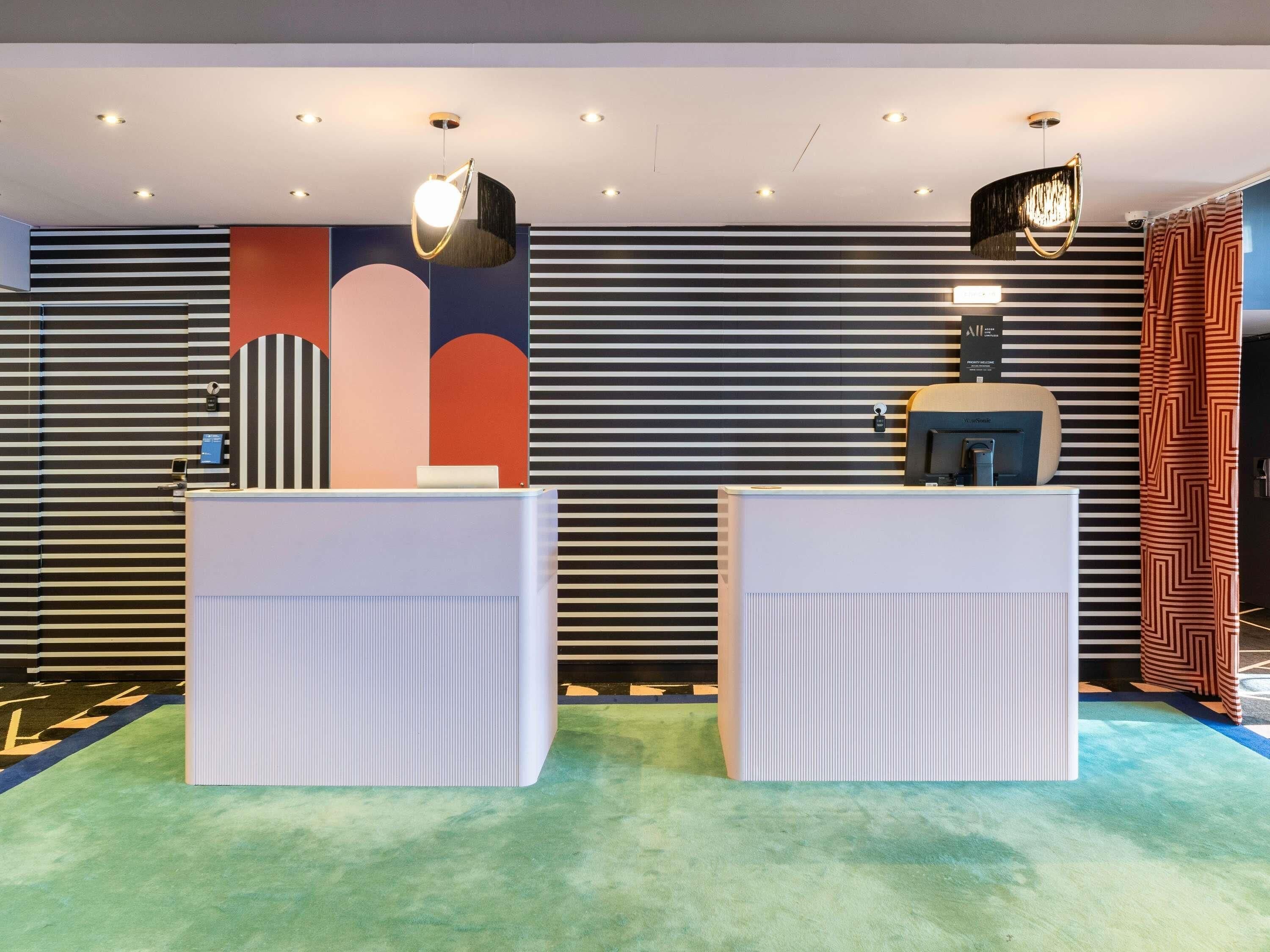 Een receptiegedeelte met twee witte balies, een moderne lamp en een patroonwand.