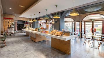 A modern cafe with a long counter, multiple hanging lights, and a view of the city through large windows.