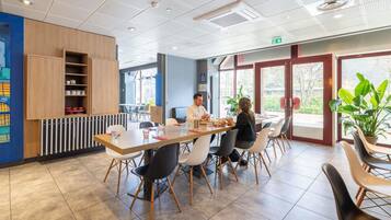 Un espace de restauration moderne, avec une longue table, des chaises et une vue dégagée grâce à de grandes fenêtres.