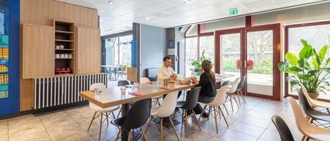 A modern dining area with a long table, chairs, and a view through large windows.