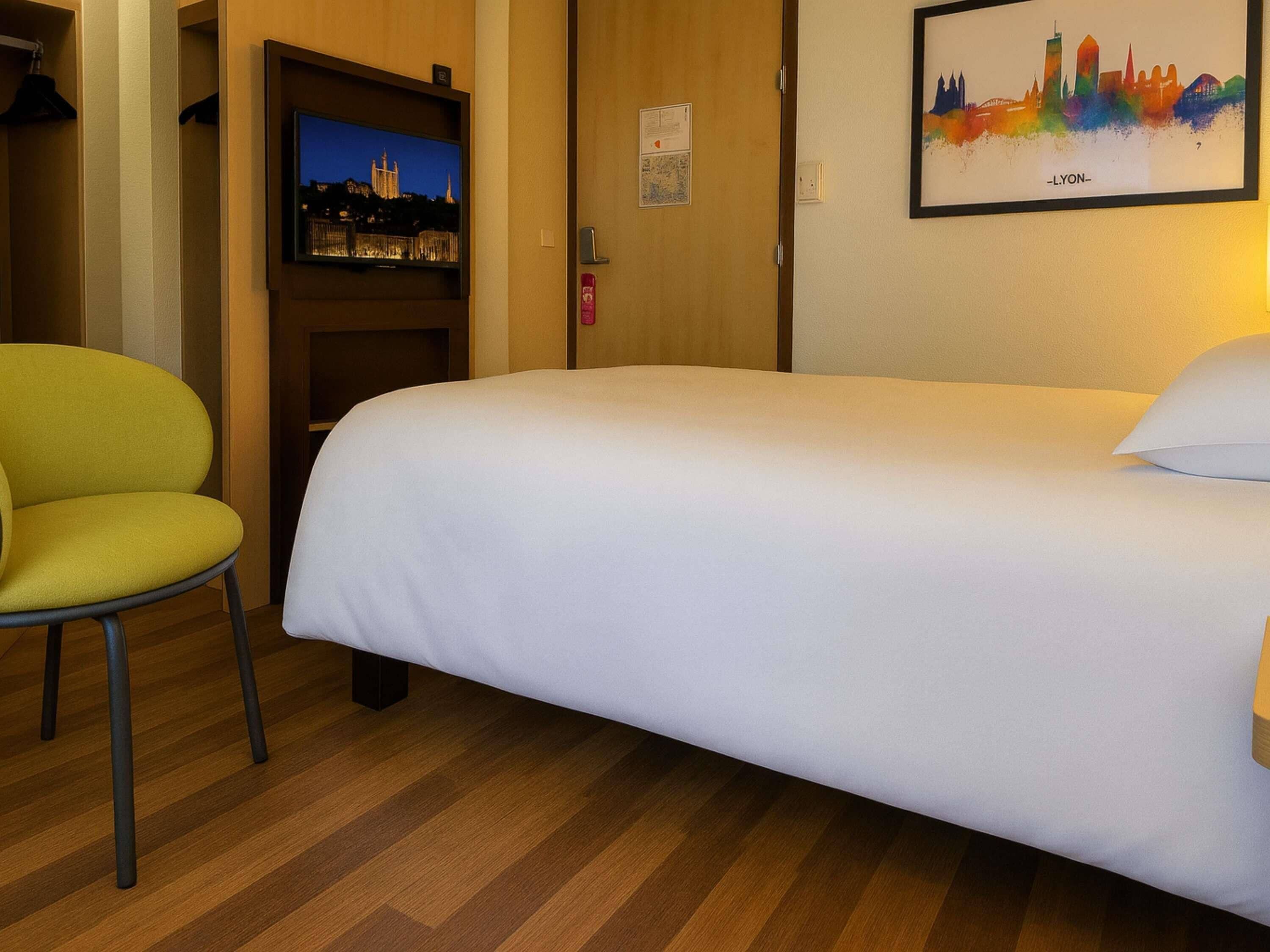 A hotel room with a bed, a chair, a television, and a cityscape painting.