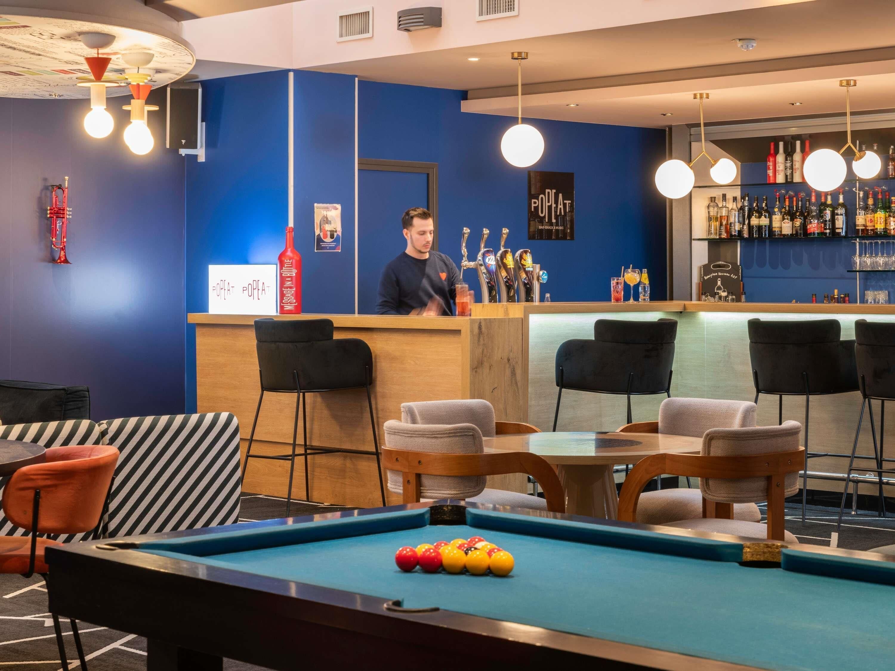 A bar area with a pool table, bar stools, and a bartender.