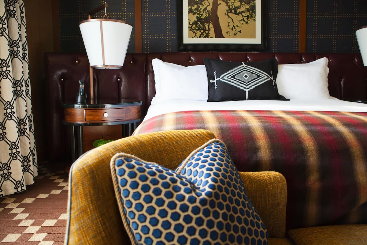 A hotel room with a large bed, a headboard, a nightstand, a lamp, and a chair with patterned cushions.