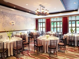 Une salle de banquet avec des tables rondes dressées pour le repas, équipées de chaises et de couverts.