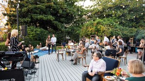 An outdoor event with a DJ setup, tables, chairs, and guests.